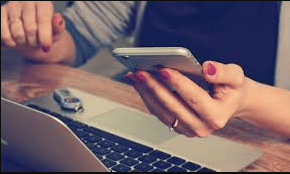 Mujer frente a una laptop con el teléfono en la mano